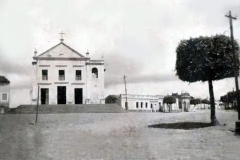 Igreja vista de frente em um largo com uma árvore
