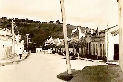 Rua antiga com casas, postes e moradores ao longe