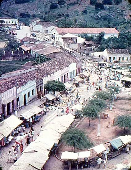 Feira movimentada entre ruas e casas, vista de um ponto elevado